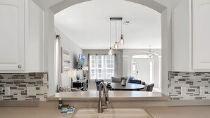 Une cuisine moderne dotée d’un îlot central, un coin repas avec une table ronde et un salon avec un canapé et un téléviseur.