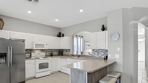 Une cuisine moderne avec des meubles blancs, des appareils en acier inoxydable et un grand îlot central doté de tabourets.
