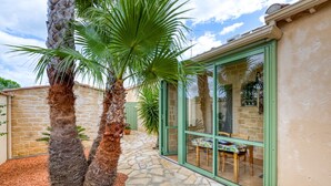 A stone pathway leading to a glass door entrance, palm trees, and a patio area with a table and chairs. - Guest Rooms 'La Palmeraie' with Sea View, Wi-Fi and Air Conditioning (Portiragnes)