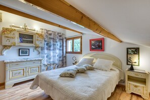 A bedroom with a bed, a nightstand, a dresser, a window, and a ceiling with exposed beams. - Guest Rooms 'La Palmeraie' with Sea View, Wi-Fi and Air Conditioning (Portiragnes)
