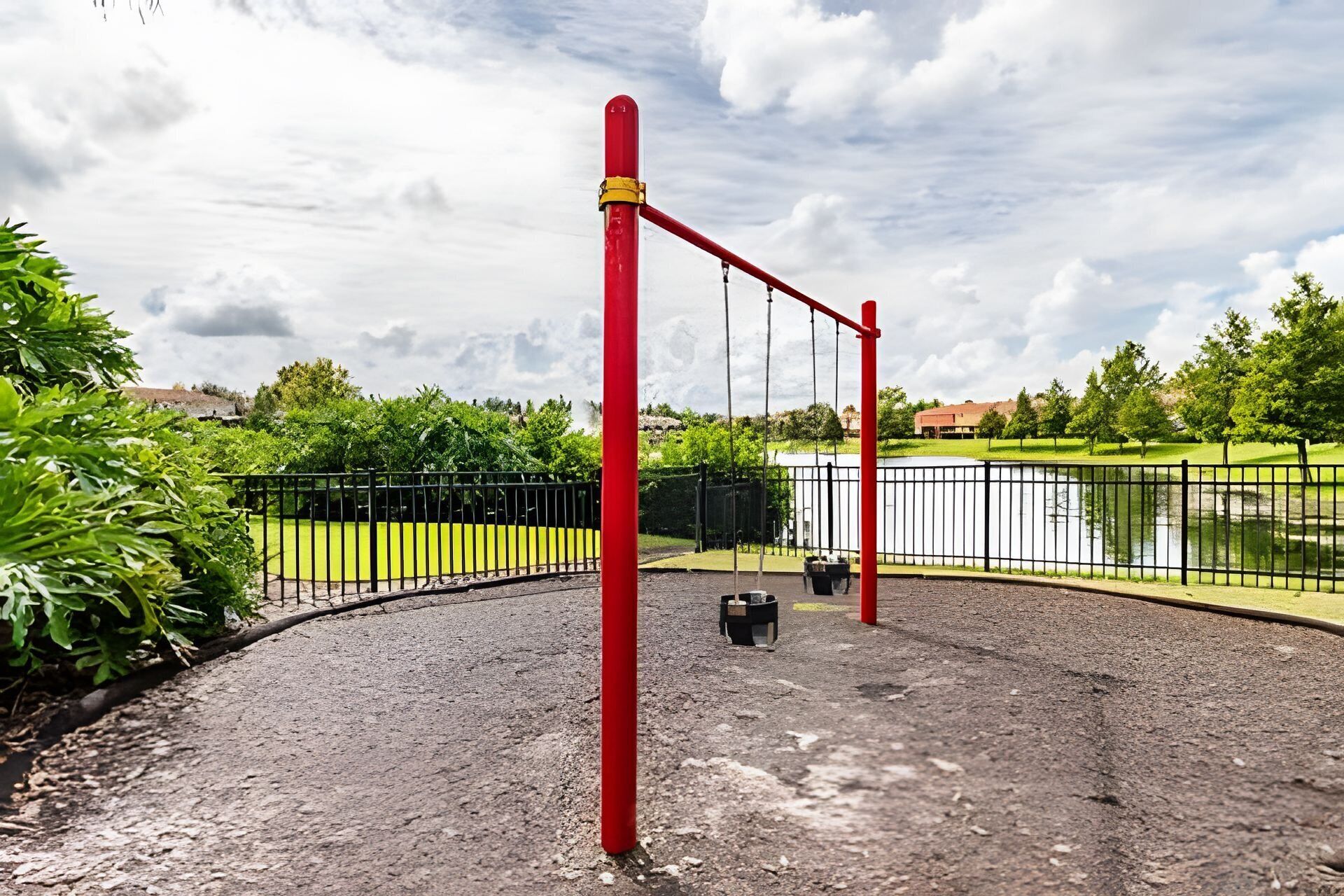 Ein Spielplatz mit roten Geräten, einer gepflasterten Fläche und einem Gewässer im Hintergrund.