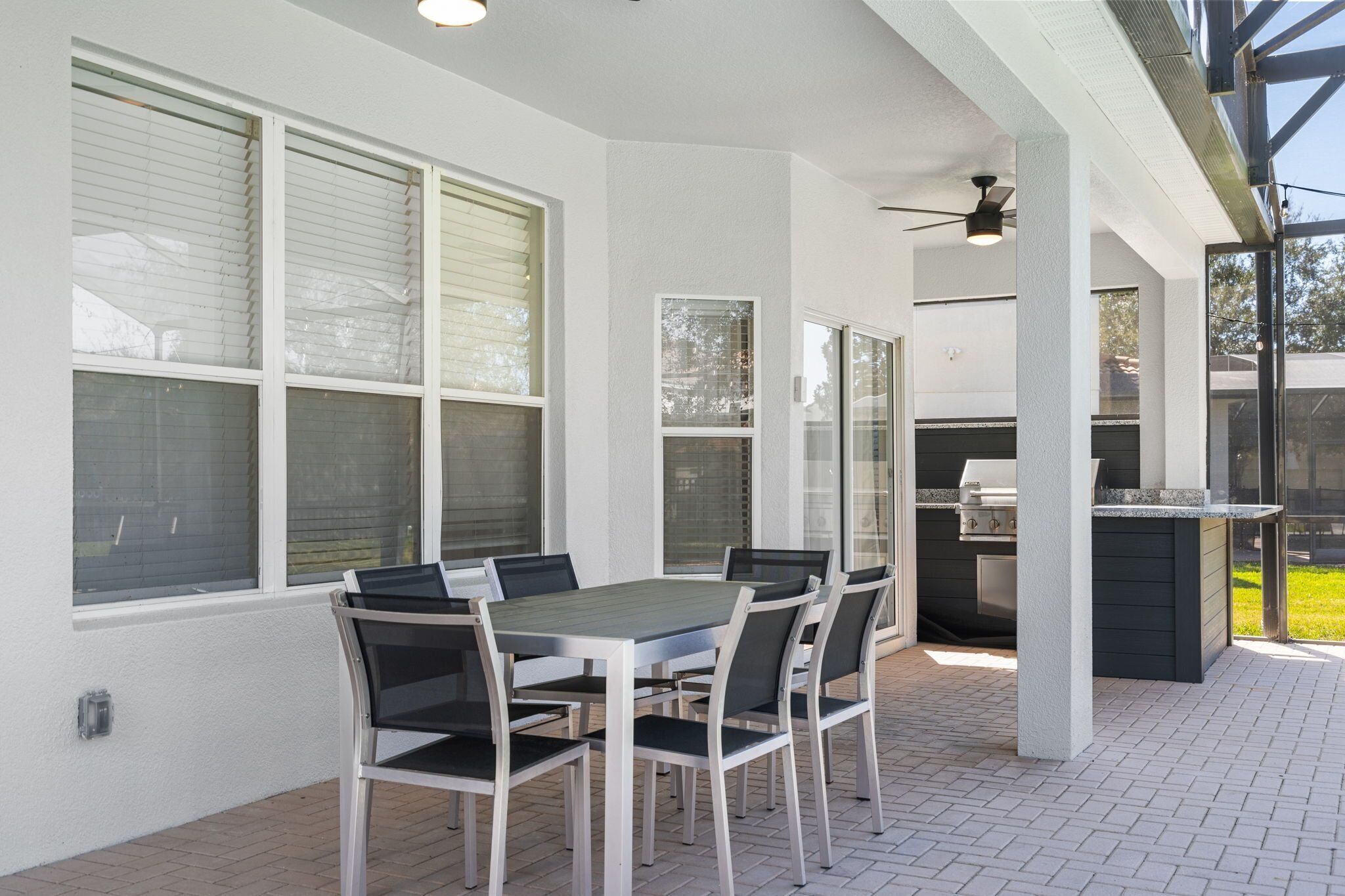 An outdoor patio with a table and chairs, a grill, and a covered area with windows.
