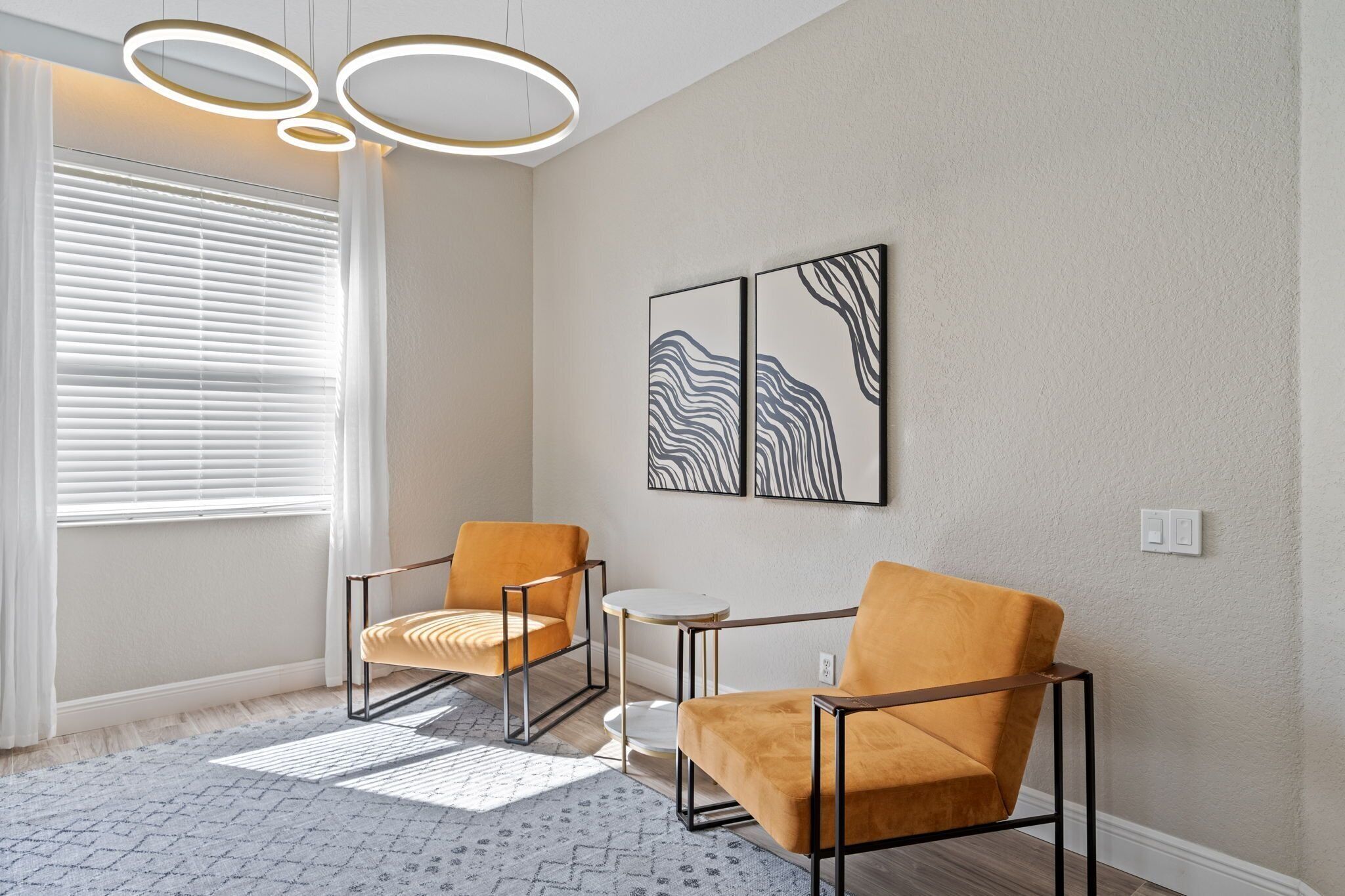 A modern living room with two armchairs, a small round table, and abstract wall art.