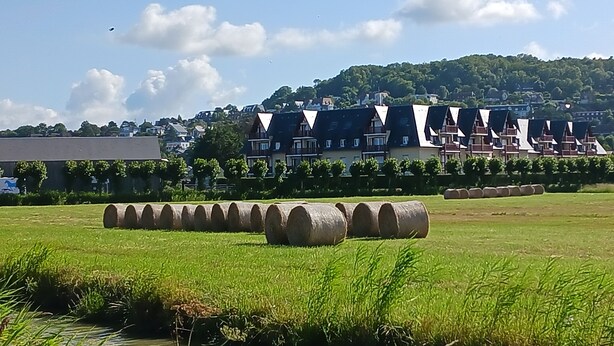 Un hôtel composé de plusieurs bâtiments à étages, avec un champ verdoyant au premier plan et un paysage vallonné en arrière-plan.