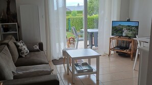 Un salon comprenant un canapé, une table basse, un téléviseur posé sur un meuble et une vue sur l’extérieur grâce à une porte vitrée.
