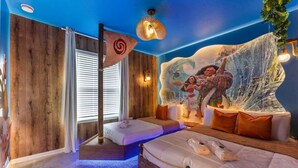 Un dormitorio con un mural de paisaje tropical, una cama con ropa de cama blanca y una pequeña zona de estar.