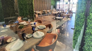 A restaurant with multiple dining tables, green walls, and a modern chandelier.