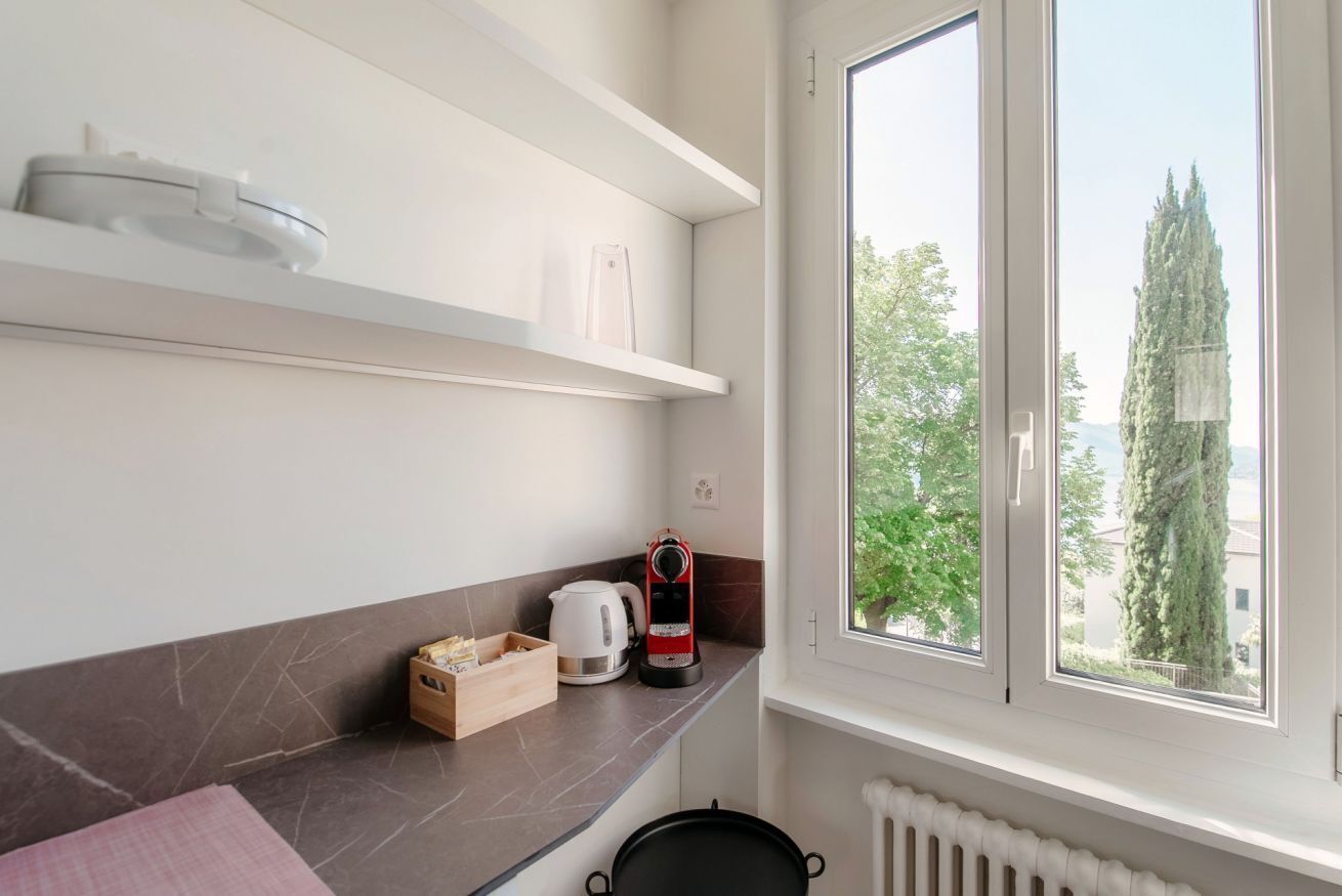 A modern kitchen with a large window, white cabinets, and a kettle on the counter.