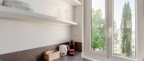 A modern kitchen with a large window, white cabinets, and a kettle on the counter.