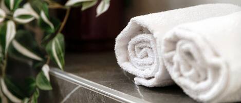 A rolled white towel on a metallic surface with a plant in the background.