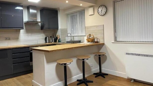 Une cuisine moderne avec des meubles de couleur sombre, un plan de travail en bois, un évier encastré et un petit îlot central avec des tabourets.