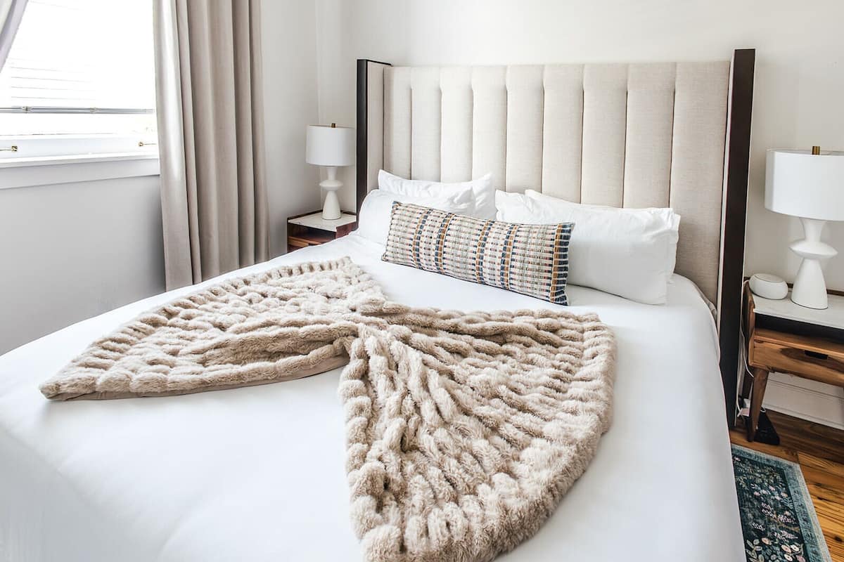 Una habitación de hotel con una cama grande, un cabecero capitonado, dos mesitas de noche con lámparas y una ventana con cortinas.
