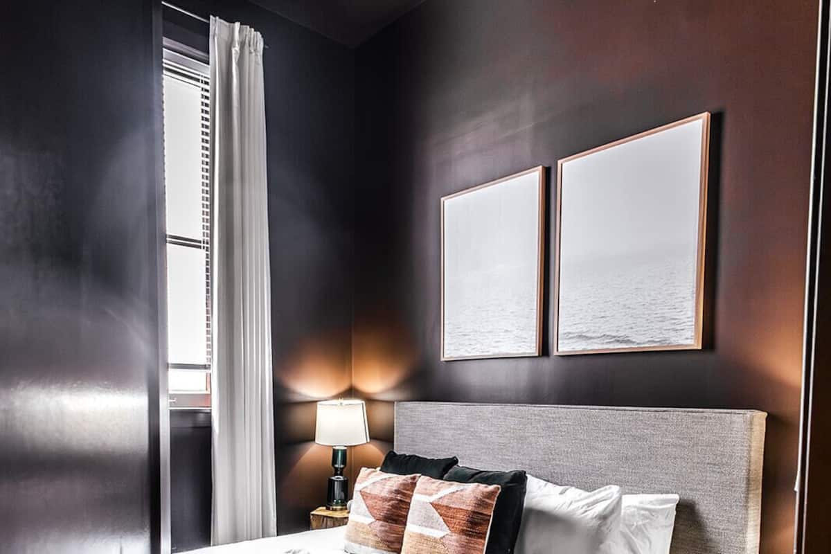 Una habitación de hotel moderna con una cama grande, una mesita de noche, una lámpara y dos cuadros en la pared.