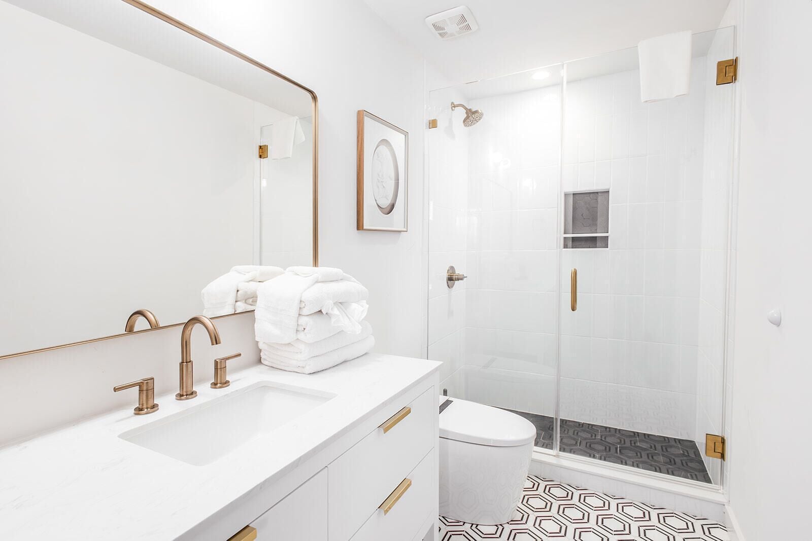A modern bathroom with a white sink, gold fixtures, a framed picture, and a shower area.