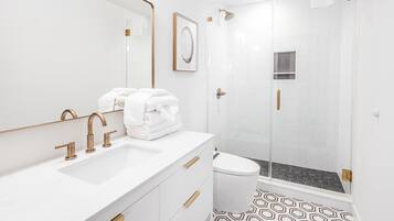 A modern bathroom with a white sink, gold fixtures, a framed picture, and a shower area.