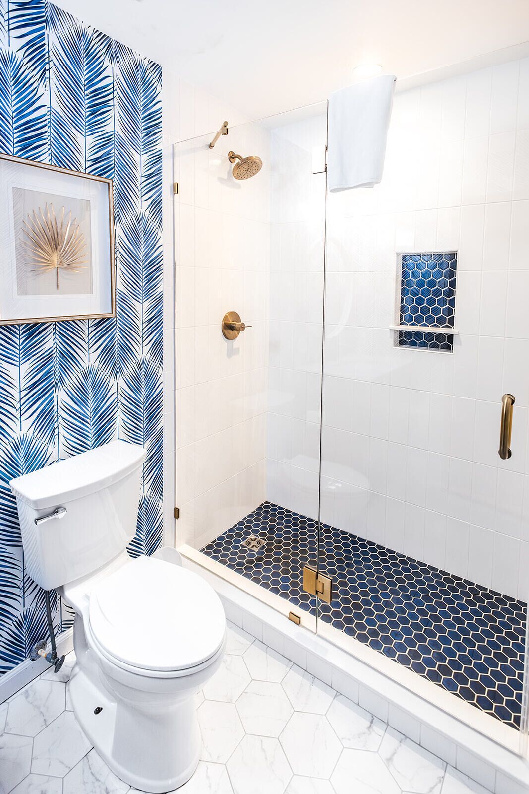 A bathroom with a toilet, shower, and a wall with a leaf pattern.