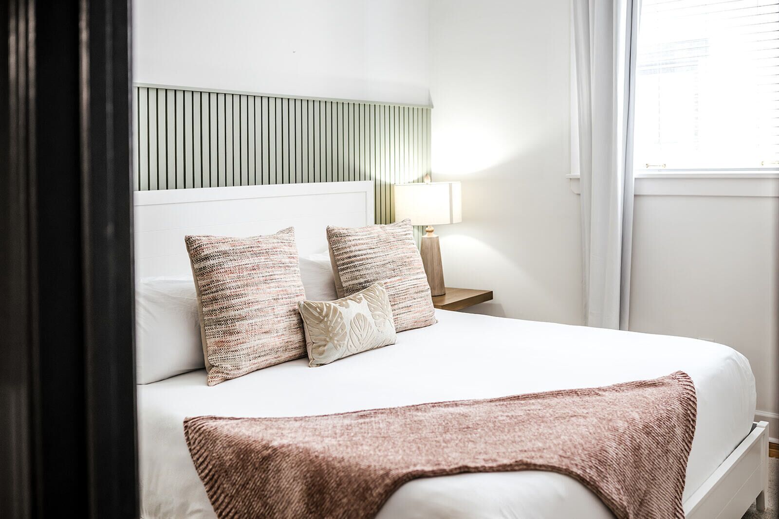 A neatly made bed with a white headboard, two patterned pillows, and a brown throw blanket.