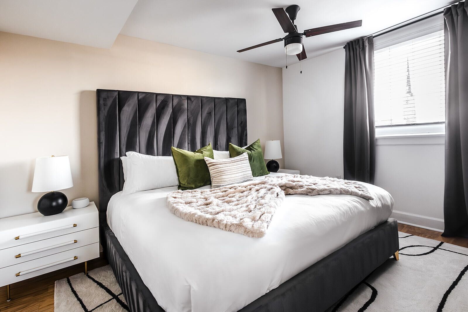 Une chambre moderne avec un grand lit, un ventilateur de plafond et une fenêtre avec des rideaux.