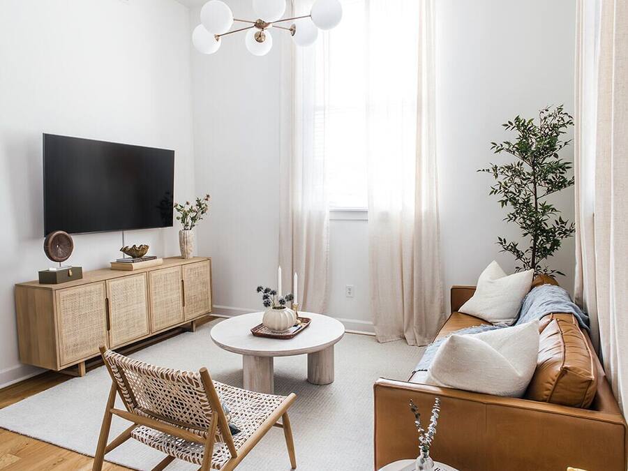 Una sala de estar moderna con una televisión de pantalla plana, una mesa de centro redonda, un sofá, una silla de mimbre y una mesita auxiliar amarilla.
