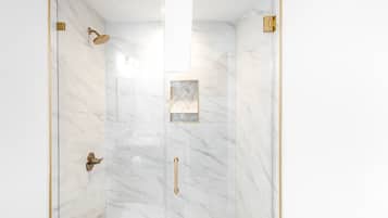 A glass-enclosed shower with marble walls and gold fixtures.