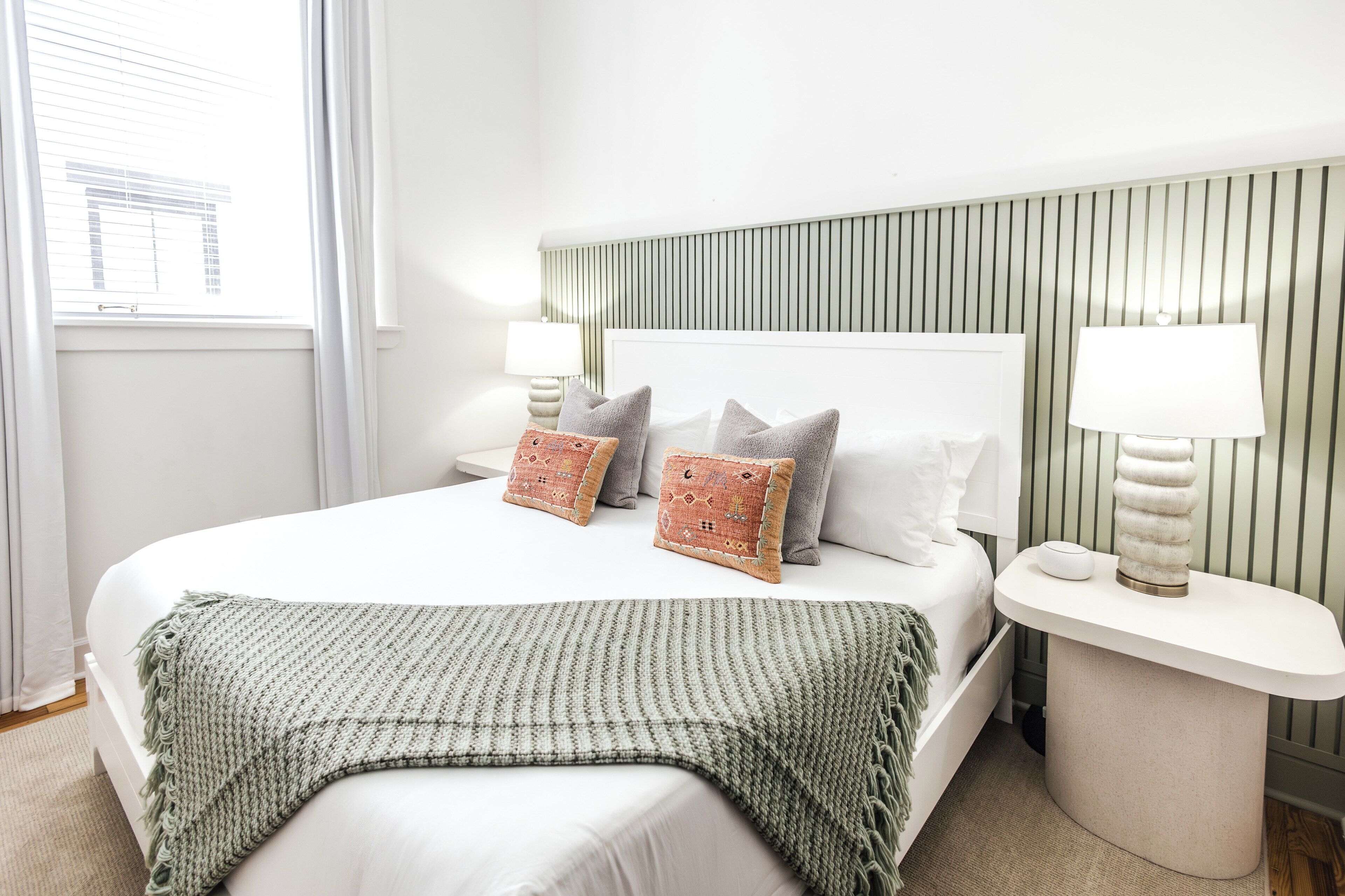 A neatly arranged bedroom with a large bed, two bedside tables with lamps, and a striped headboard.