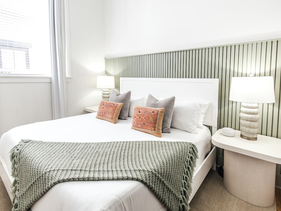 Un dormitorio ordenado con una cama grande, dos mesitas de noche con lámparas y un cabecero a rayas.