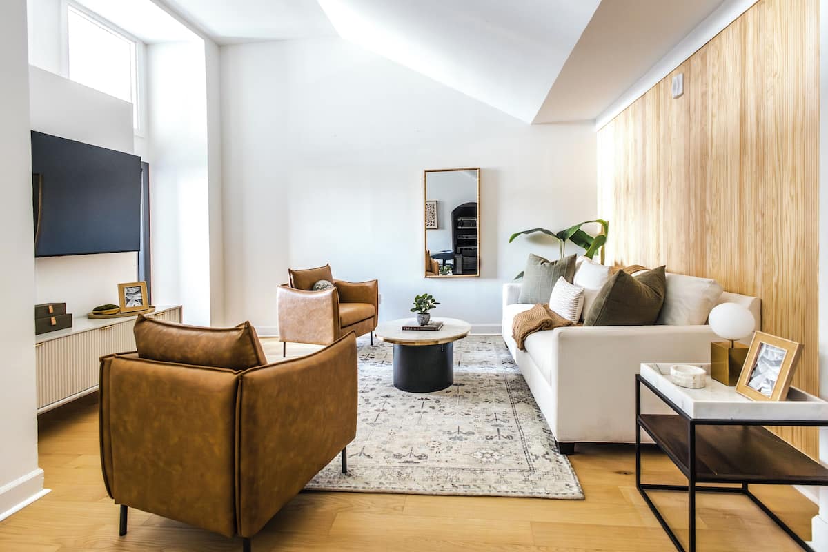 Una sala de estar moderna con sofá, sillón, mesa de centro y televisor montado en la pared.