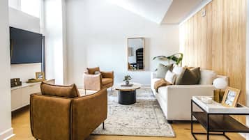 Una sala de estar moderna con sofá, sillón, mesa de centro y televisor montado en la pared.