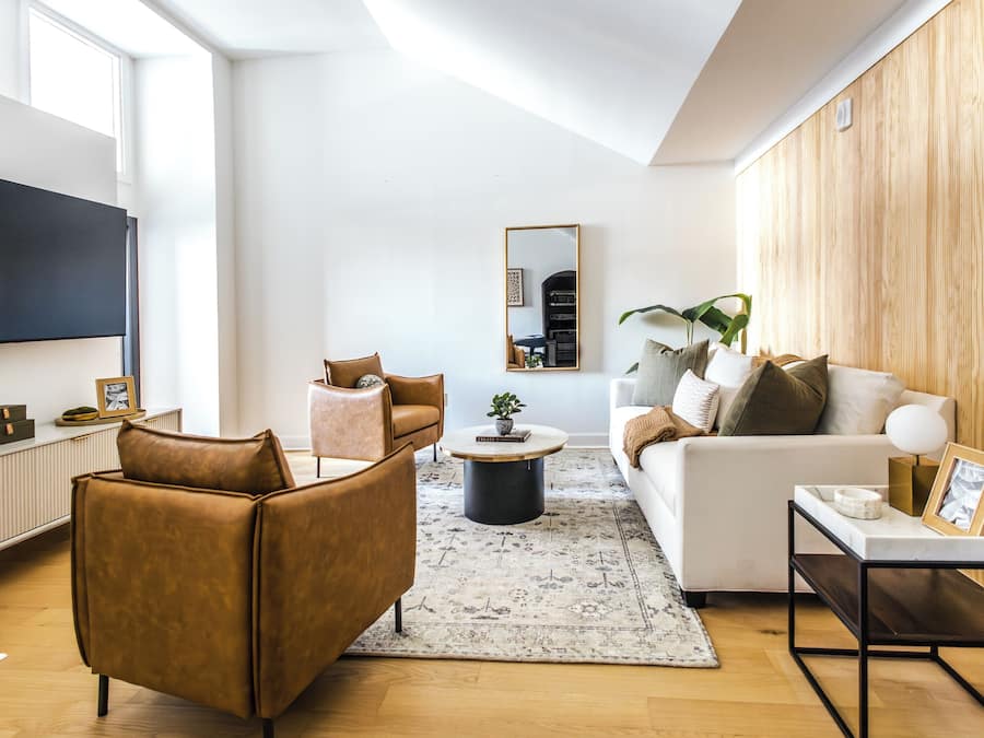 Una sala de estar moderna con sofá, sillón, mesa de centro y televisor montado en la pared.