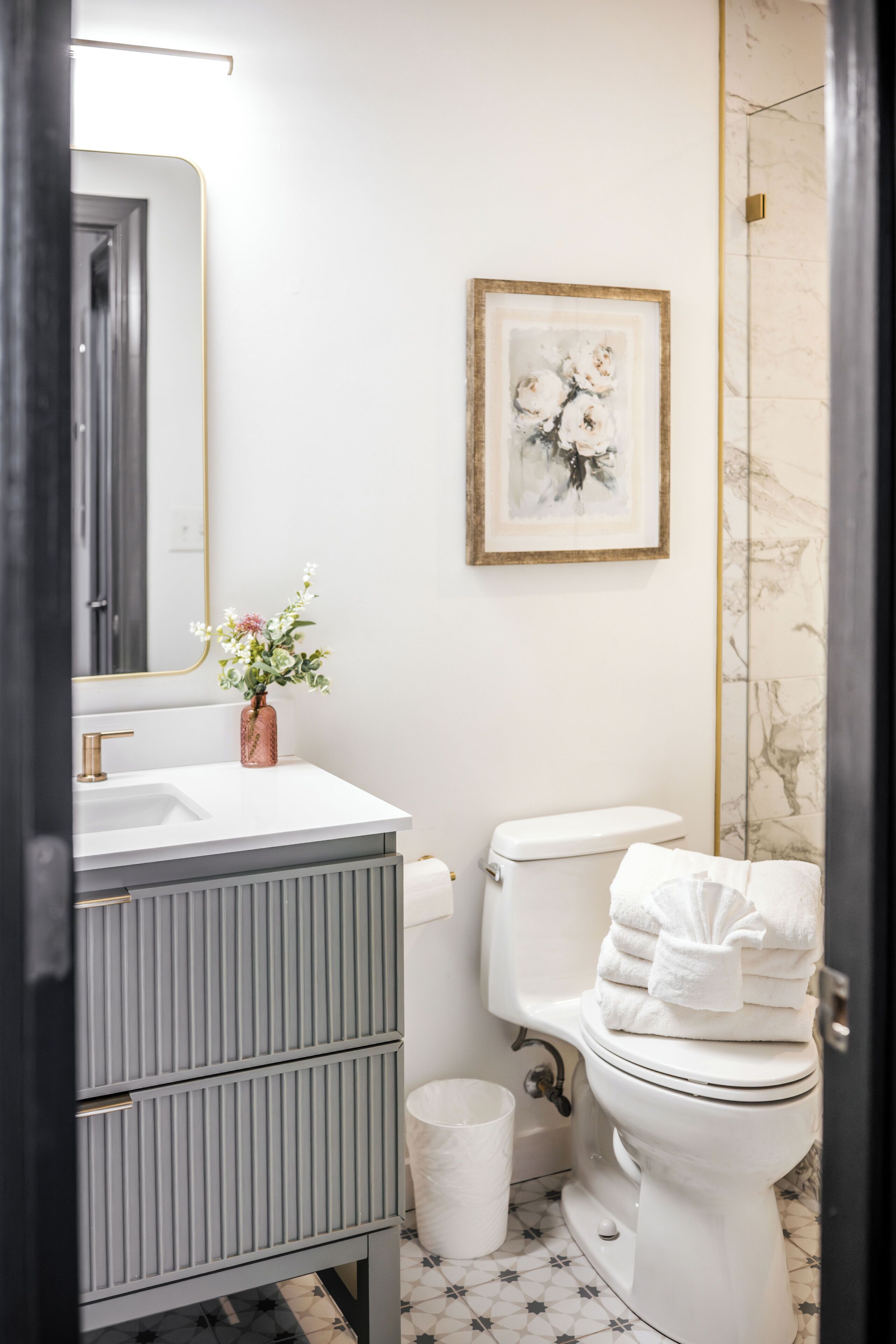 A bathroom with a white sink, a toilet, a framed artwork on the wall, and a small trash bin.