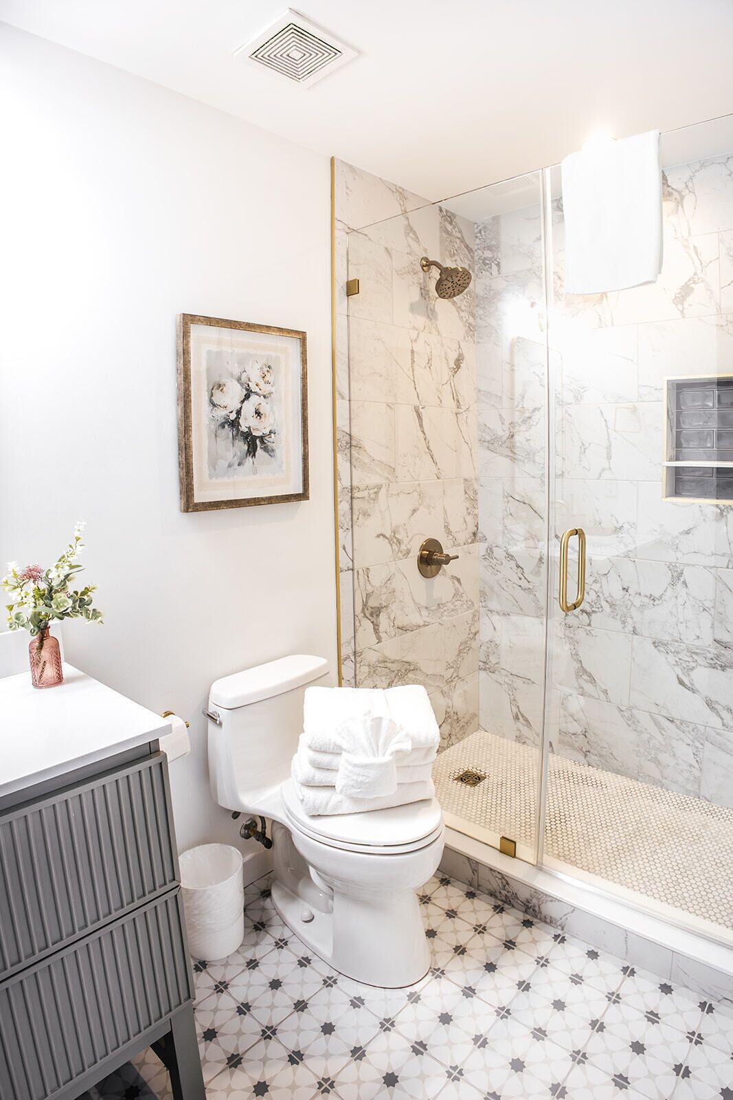 A bathroom with a toilet, a shower with glass doors, a marble wall, and a framed picture on the wall.