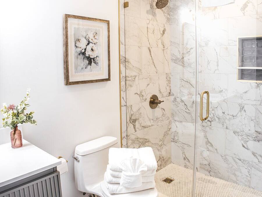A bathroom with a toilet, a shower with glass doors, a marble wall, and a framed picture on the wall.