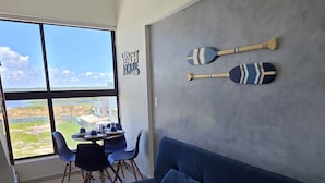 A modern living room with a large window, a blue sofa, and two paddles on the wall. - Duplex 303B belavista by la playa (Ipojuca)
