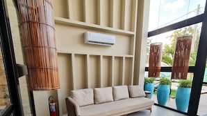 A modern lounge area with a sofa and a wicker chair, a wall-mounted air conditioner, and potted plants. - Duplex 303B belavista by la playa (Ipojuca)