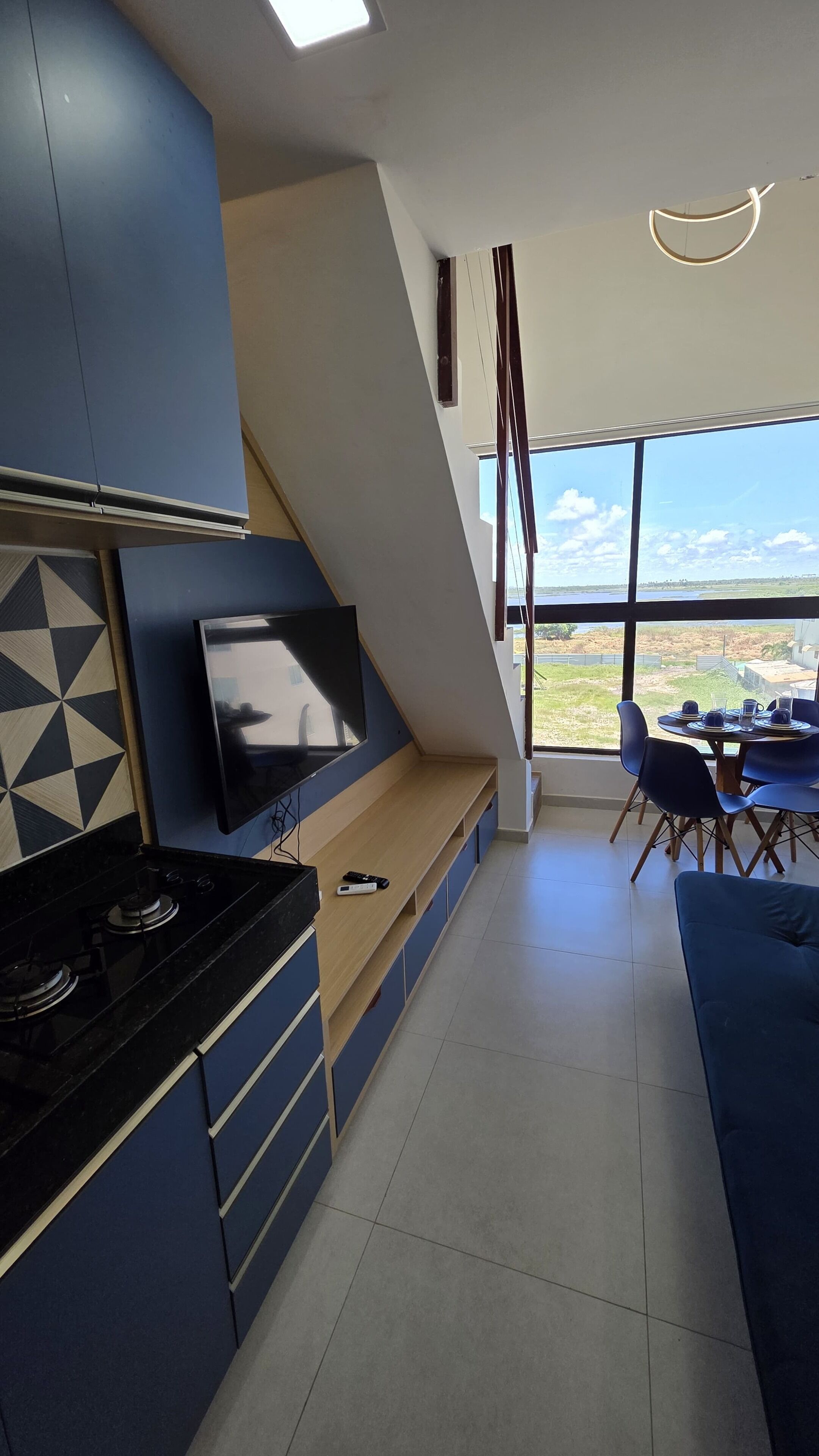 A modern kitchen with a built-in TV, a dining area with a table and chairs, and a large window offering a view of the outdoors.