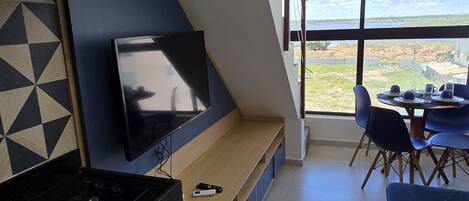 A modern kitchen with a built-in TV, a dining area with a table and chairs, and a large window offering a view of the outdoors.