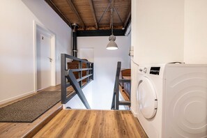 Een wasruimte met een wasmachine, een houten trap en een deur met het nummer 2.
