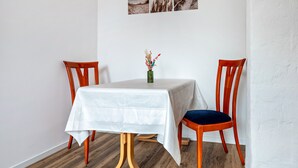 A dining area with a table covered in a white tablecloth, two wooden chairs, and a vase with dried flowers.