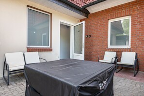 A covered outdoor patio with a table and four chairs, brick walls, and large windows.