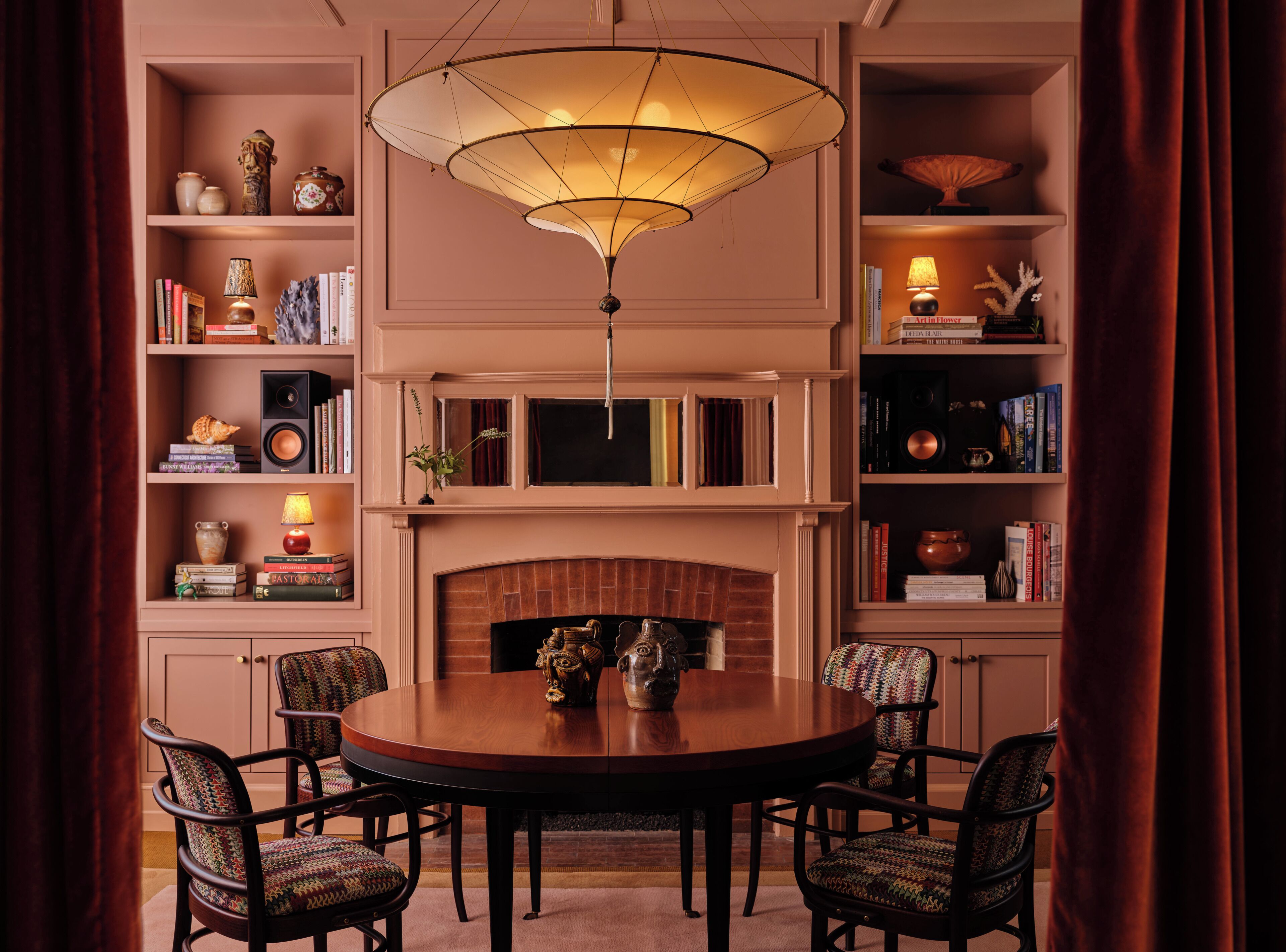 A dining area with a round table, four chairs, a fireplace, and bookshelves with various items.