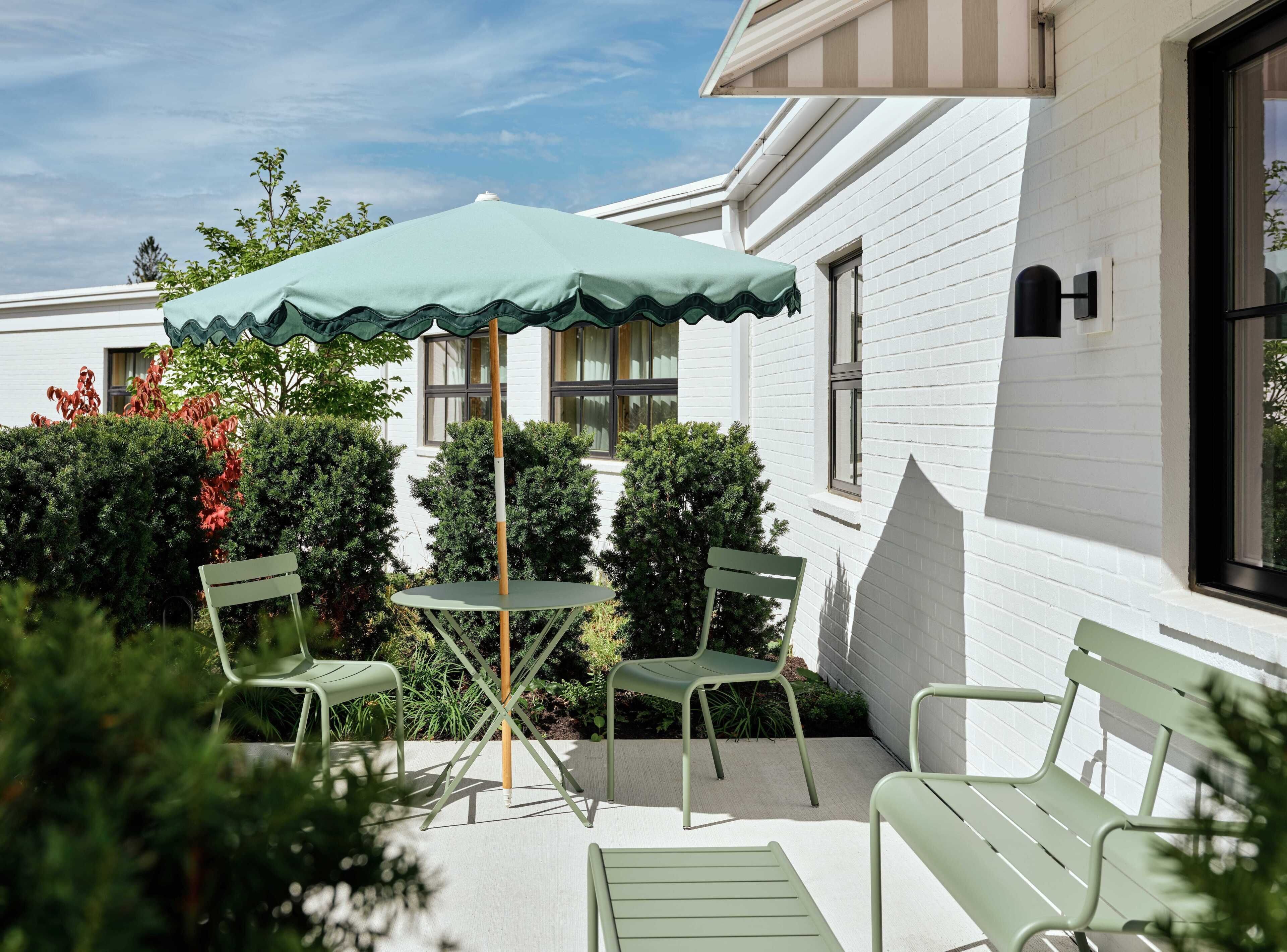 A patio with a table and chairs, an umbrella, and a white building with windows.