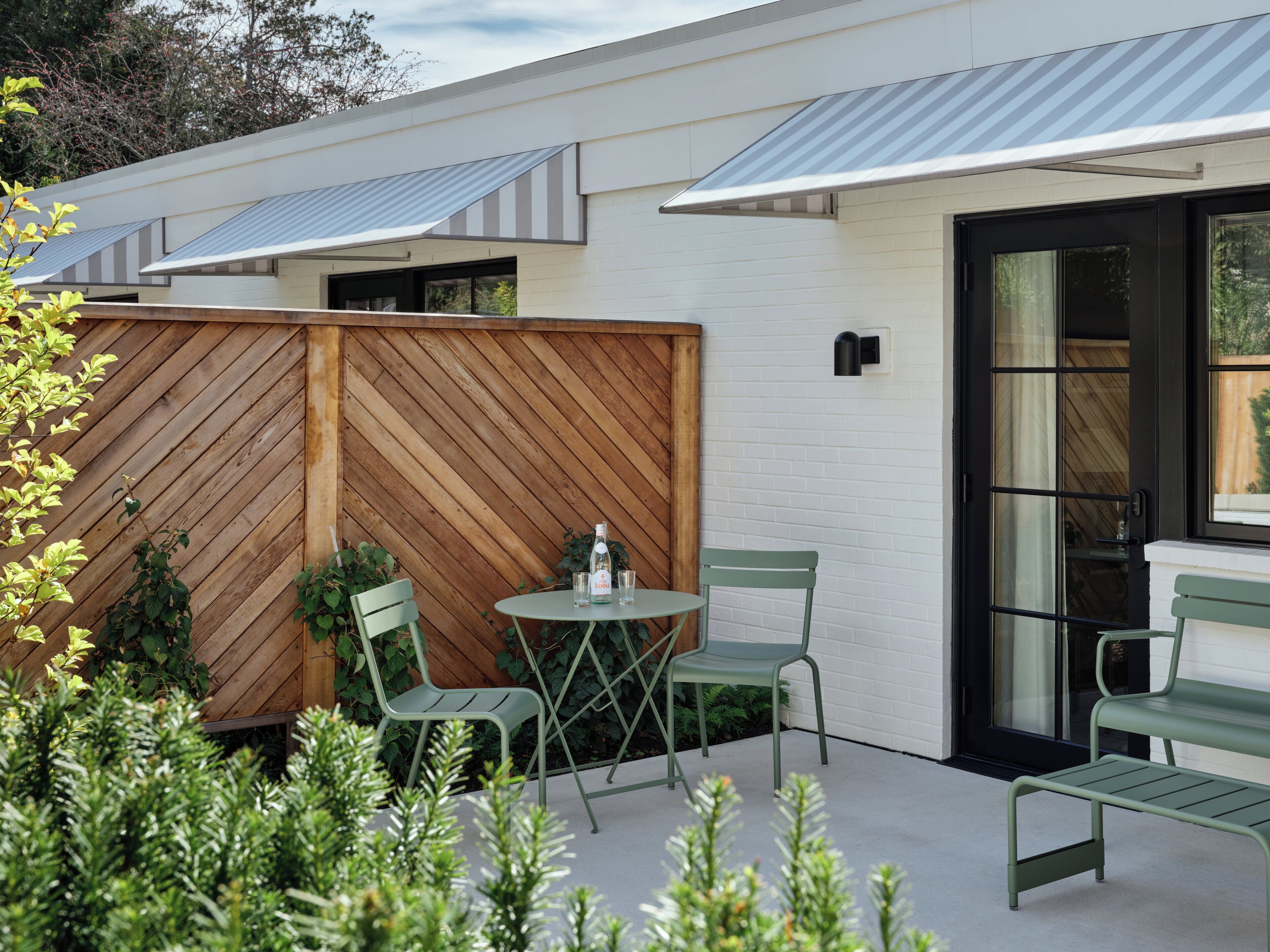 A patio with two green chairs, a small round table, and a wooden fence.