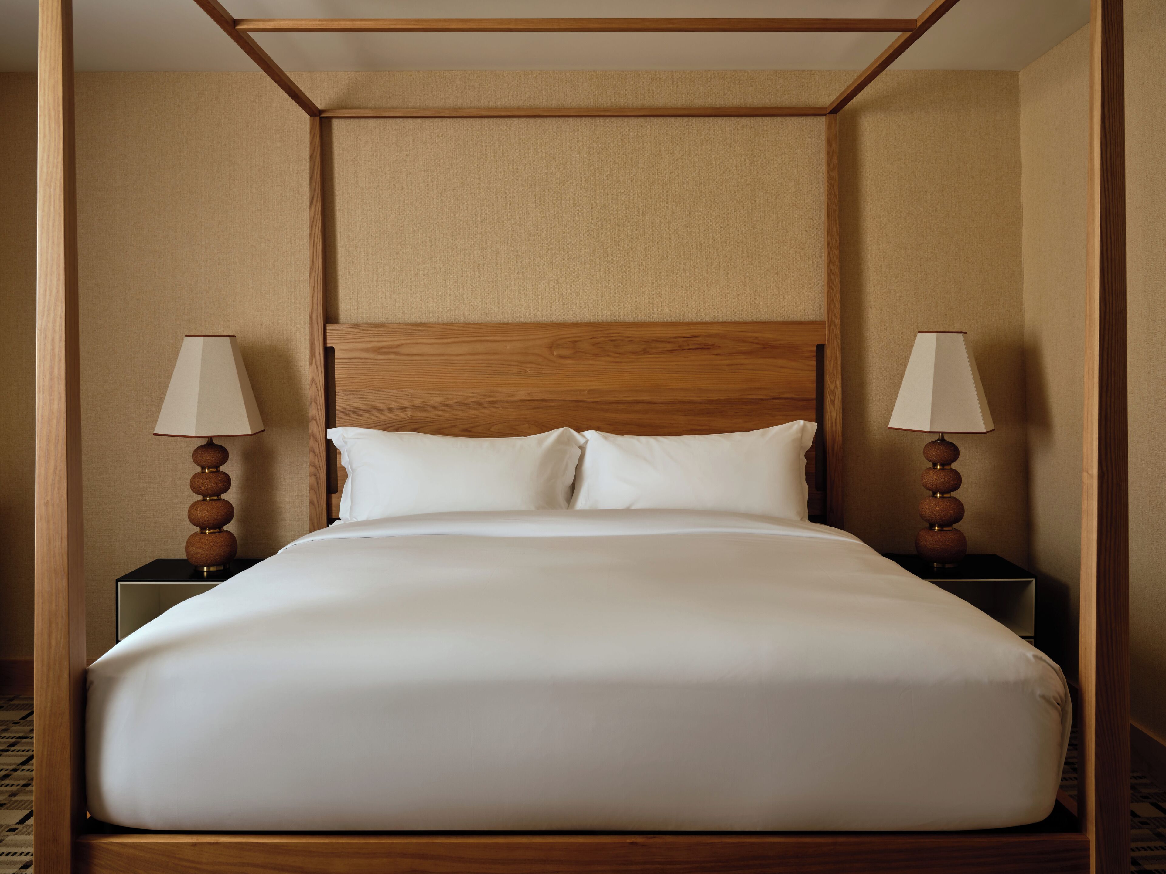 A hotel room with a wooden four-poster bed, white linens, and two bedside lamps.
