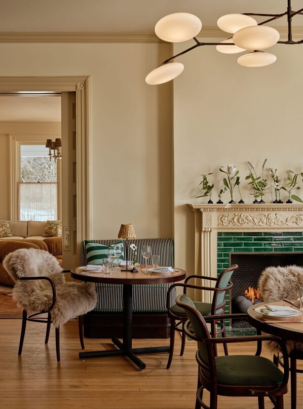 Un comedor con una mesa redonda, sillas, chimenea y diversas plantas.