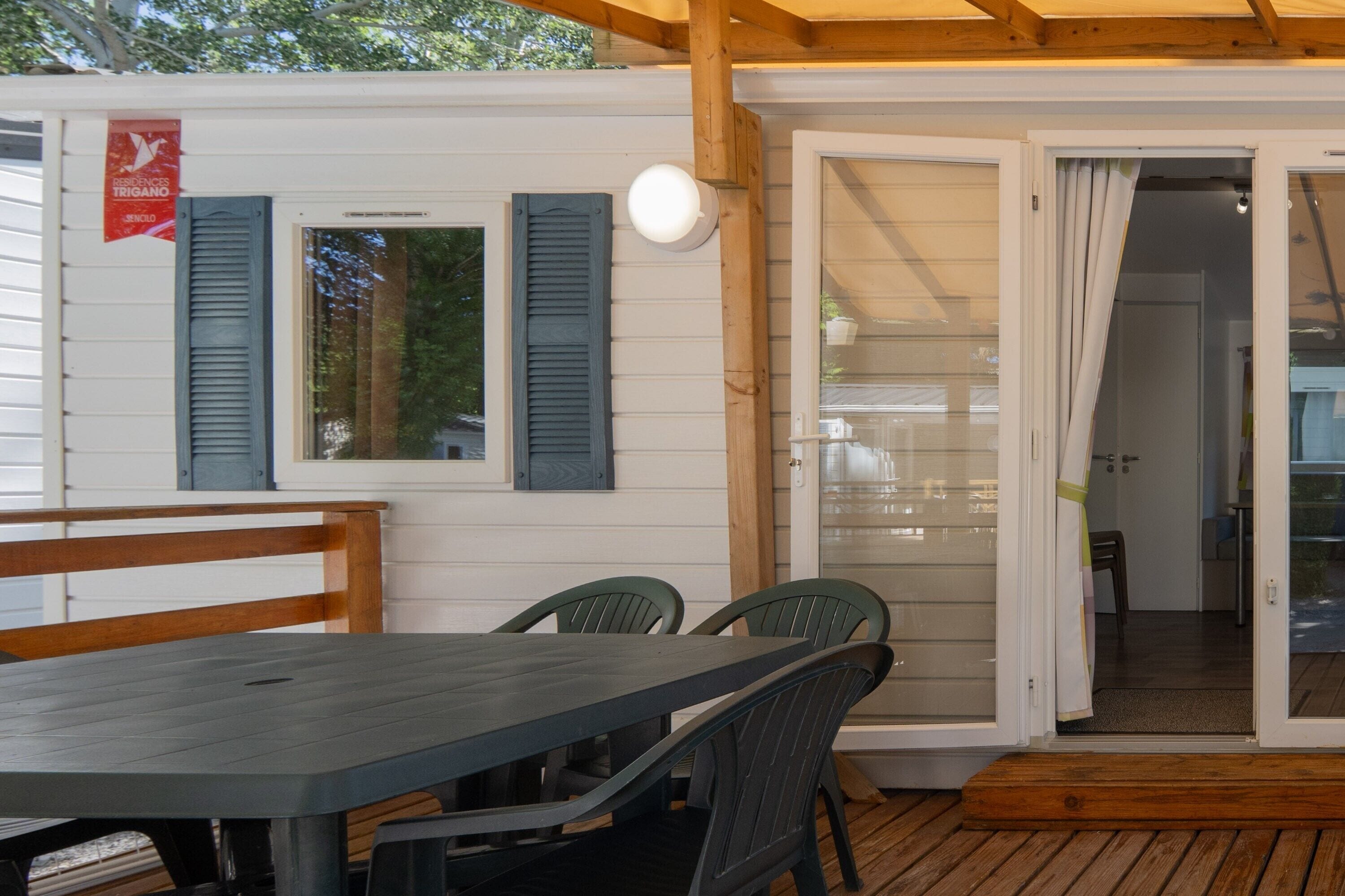 Een overdekt terras met een tafel en stoelen, een houten bank en een deur naar binnen.