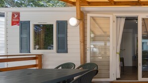 A covered patio with a table and chairs, a wooden bench, and a door leading inside. - Mobile Home 'Confort B - 1-5 Persons' with Shared Pool, Private Terrace and Communal Garden (Lavilledieu)