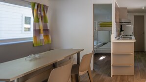 A modern kitchen with a built-in stove, a white countertop, and a window with curtains. - Mobile Home 'Confort B - 1-5 Persons' with Shared Pool, Private Terrace and Communal Garden (Lavilledieu)