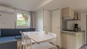 A compact kitchen with a dining area, a built-in stove, and a window with curtains. - Mobile Home 'Confort B - 1-6 Pers' with Shared Pool, Private Terrace and Shared Garden (Lavilledieu)