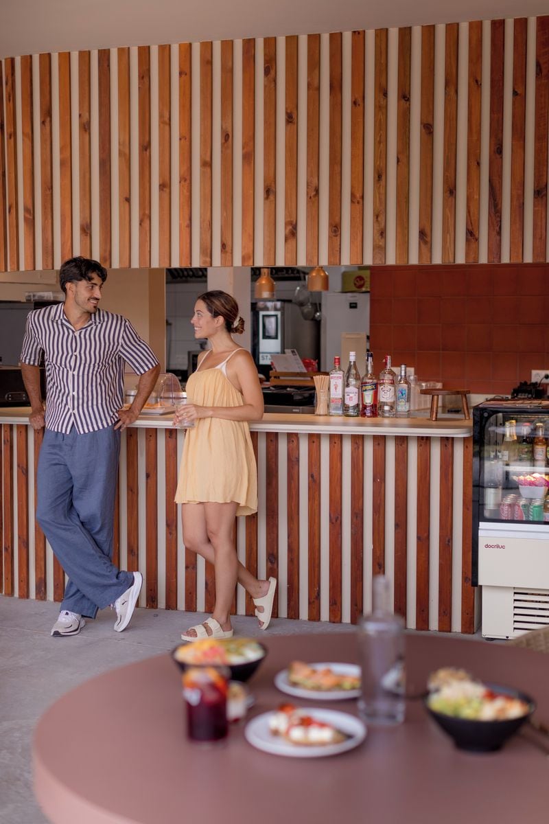 Zona de bar con pared de listones de madera, mostrador con botellas y nevera con alimentos.