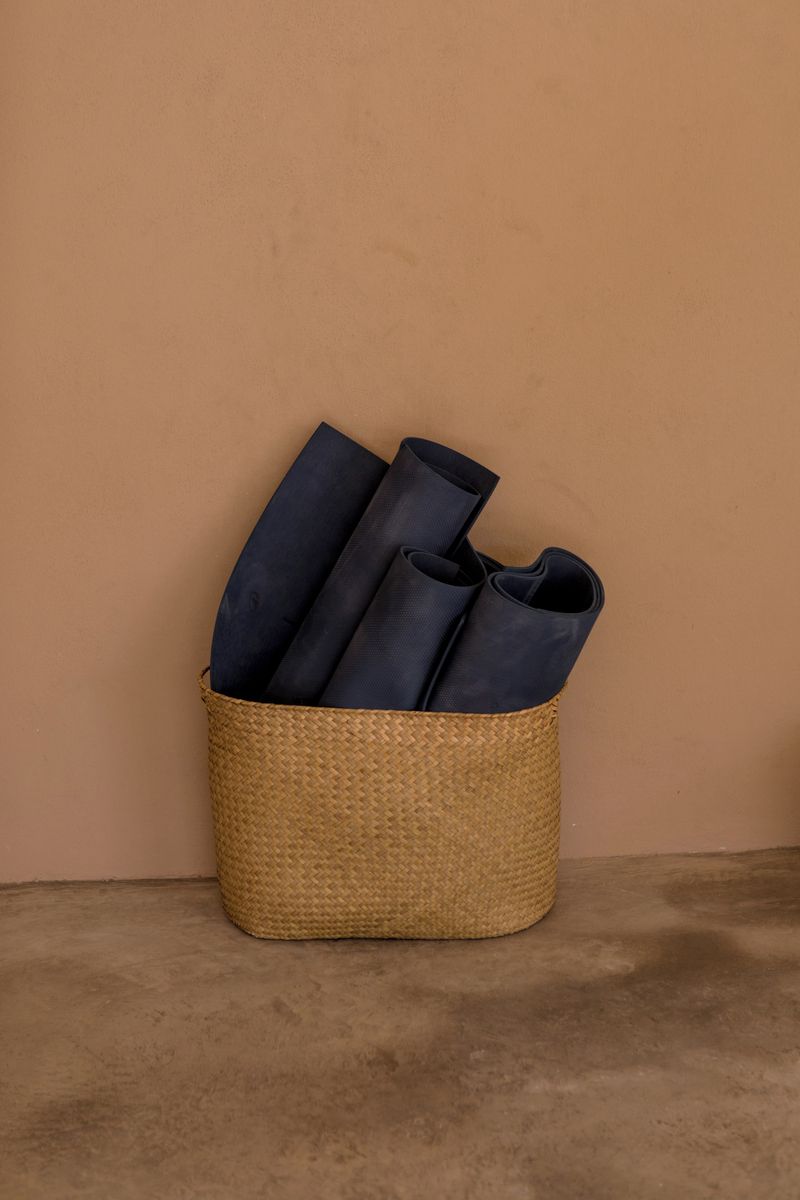 Una cesta tejida con objetos enrollados frente a una pared lisa.